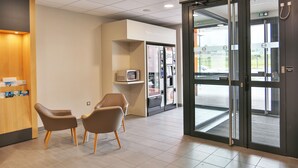 A reception area with a counter, two chairs, a microwave, and a vending machine. - B&B HOTEL LES HERBIERS (Les Herbiers)