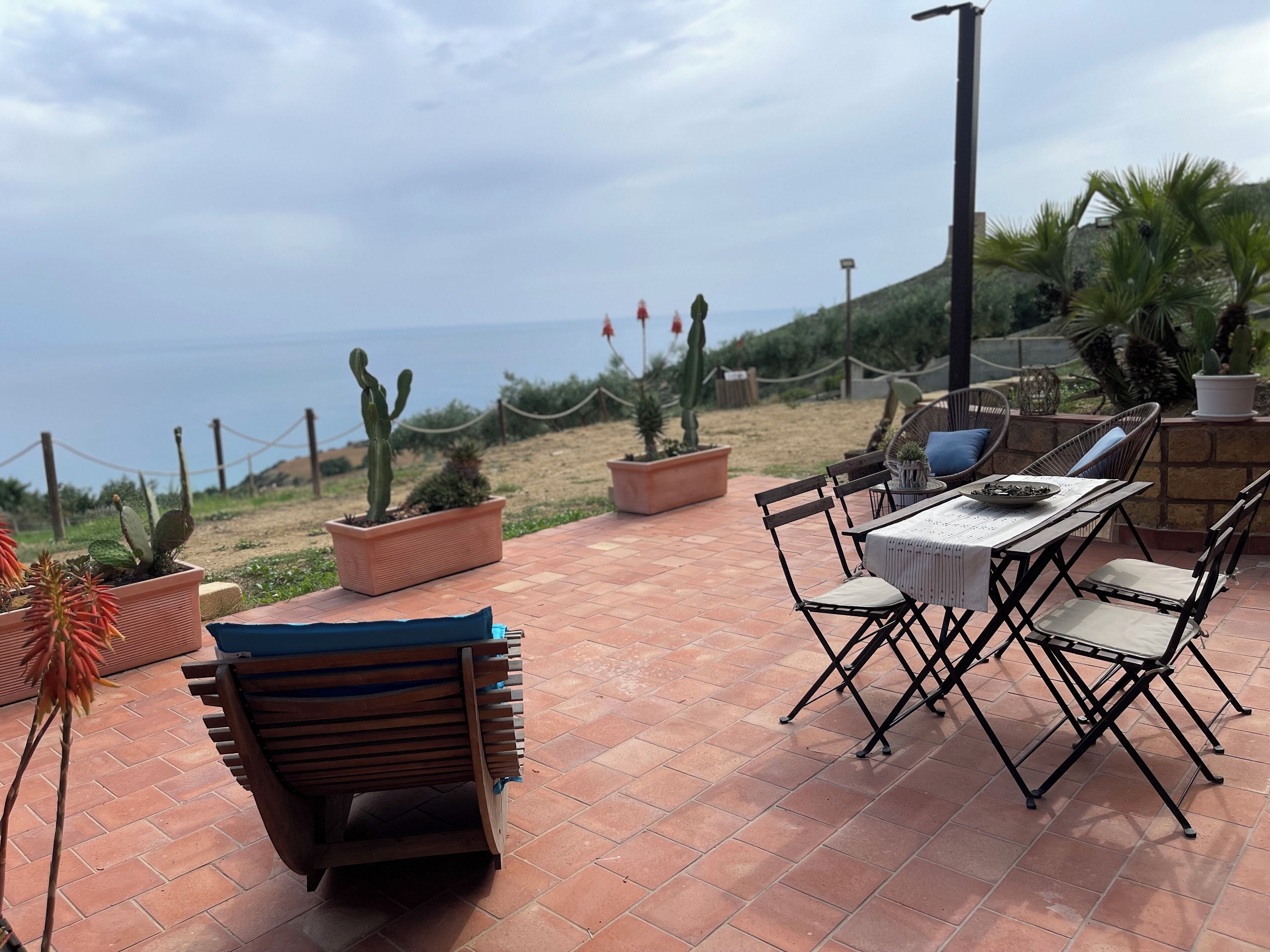 Une terrasse extérieure avec une table et des chaises, entourée de plantes en pot et offrant une vue sur la mer.