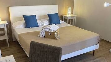 A neatly made bed with blue pillows, a bedside table with a lamp, and a painting of a coastal scene on the wall.