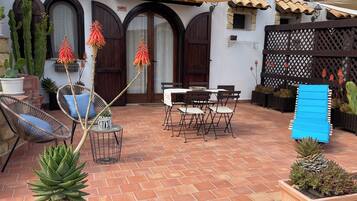 A patio with a table and chairs, surrounded by potted plants and a wooden fence.