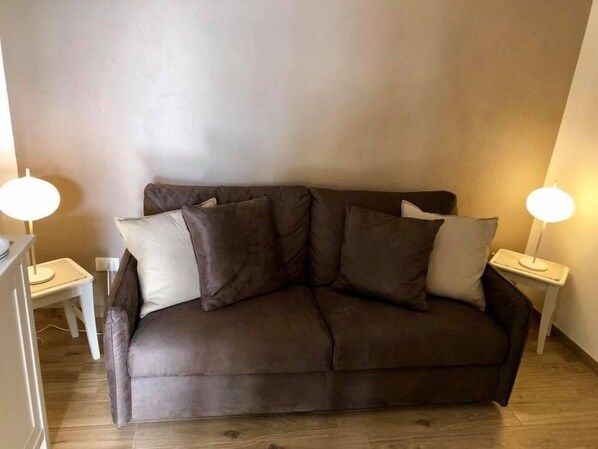 A brown sofa with multiple cushions, two bedside tables with lamps, and a wooden floor.