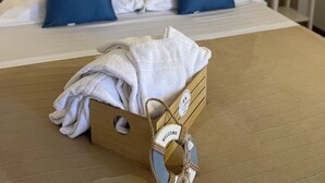 Un lit bien fait, agrémenté d’oreillers bleus, un plateau en bois avec des serviettes et un panneau d’accueil.