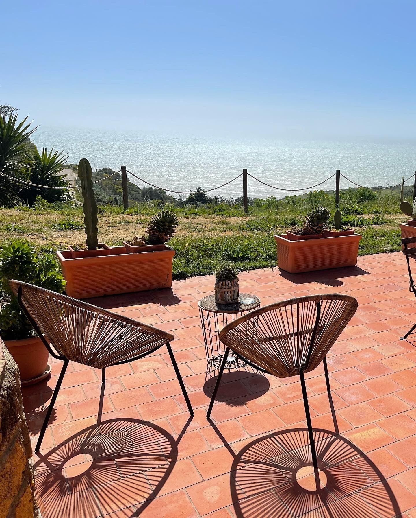 A terrace with wicker chairs and potted plants overlooking the sea.