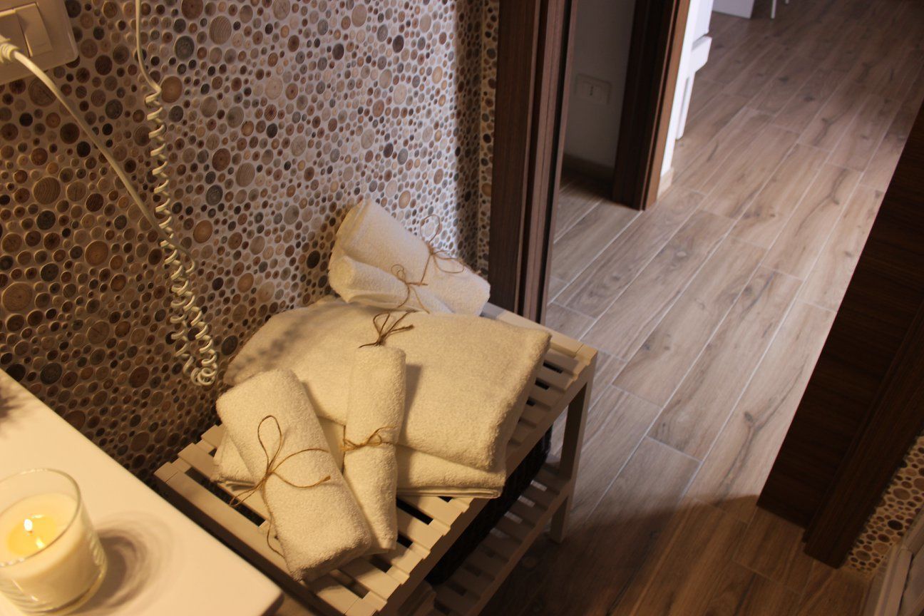 Un banco de madera con toallas y una vela en una habitación con pared texturizada y suelo de madera.