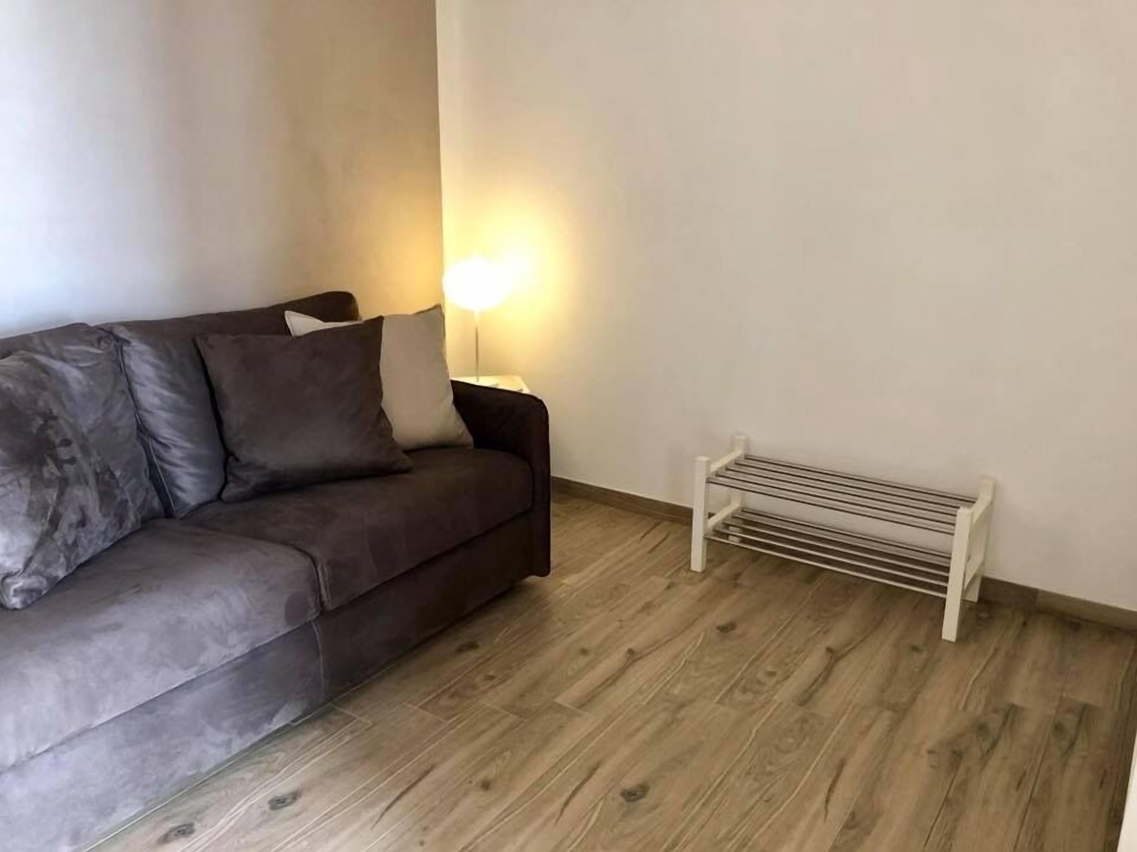 Una sala de estar con un sofá marrón oscuro, un radiador blanco y suelo de madera.