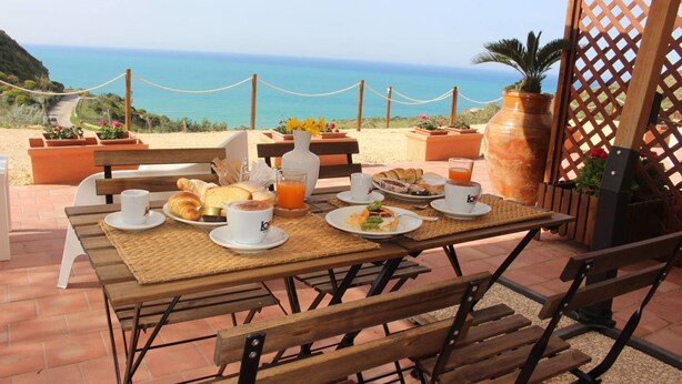 Un espace extérieur aménagé pour prendre les repas, avec une table dressée pour le petit-déjeuner, offrant une vue sur la côte.