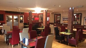 Un restaurant avec des banquettes et des tables, des chaises rouges et blanches, et des piliers en briques.
