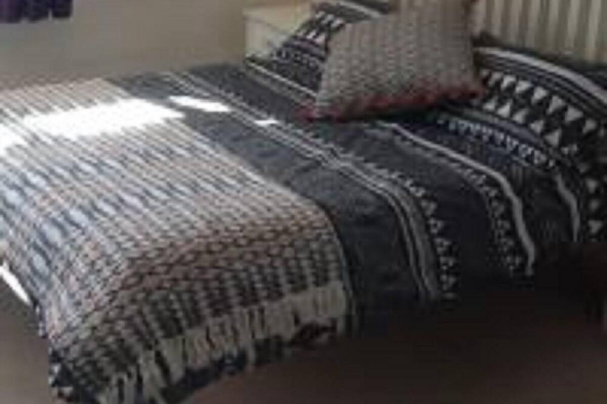 A bed with a patterned bedspread and pillows, a white headboard, and a window with curtains.