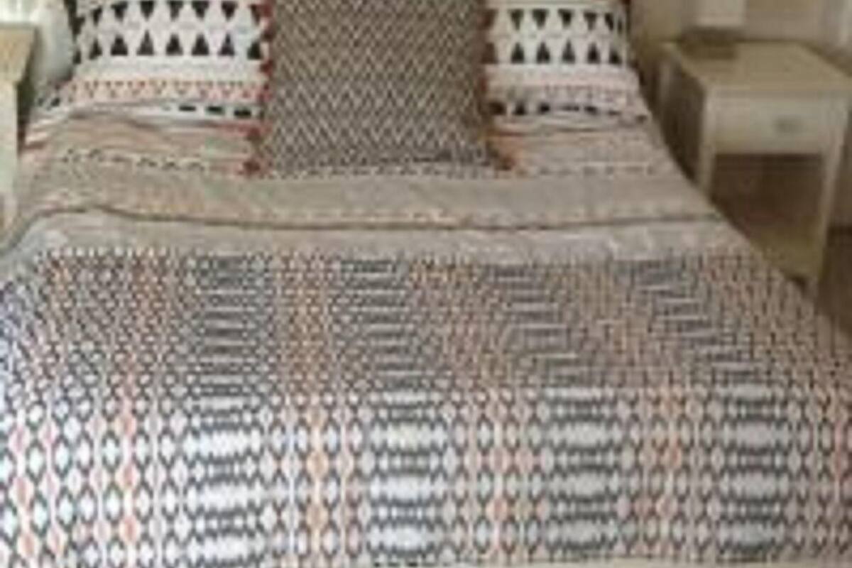 A bed with a patterned bedspread and pillows, a wooden headboard, and a nightstand with a lamp.