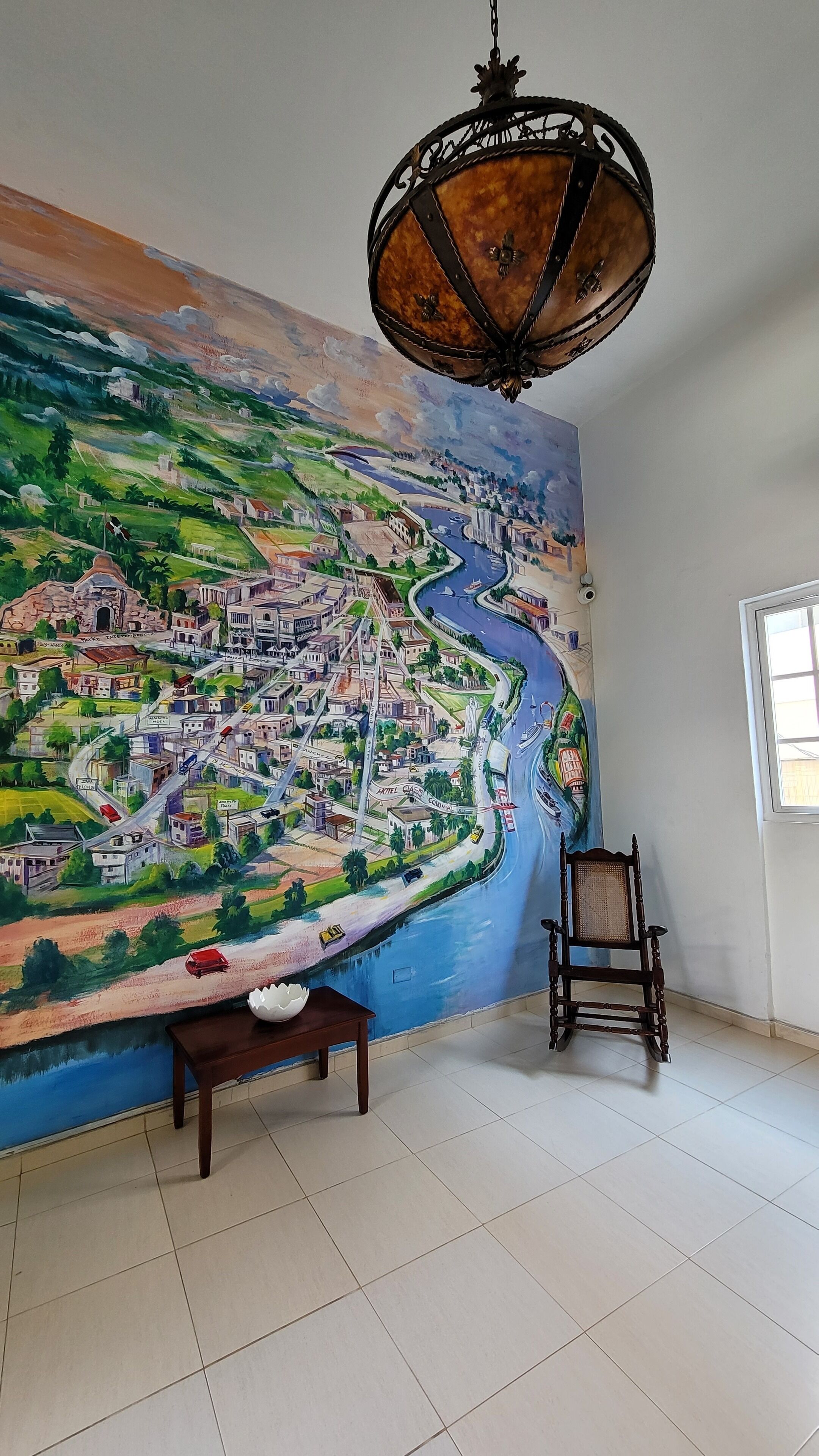 Una stanza con un grande murale raffigurante una città e un fiume, una panca di legno e una sedia.