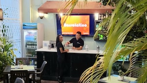 An outdoor restaurant with tables and chairs, a bar area with a counter, and a refrigerator stocked with beverages. - Hotel Class Colonial (Santo Domingo)