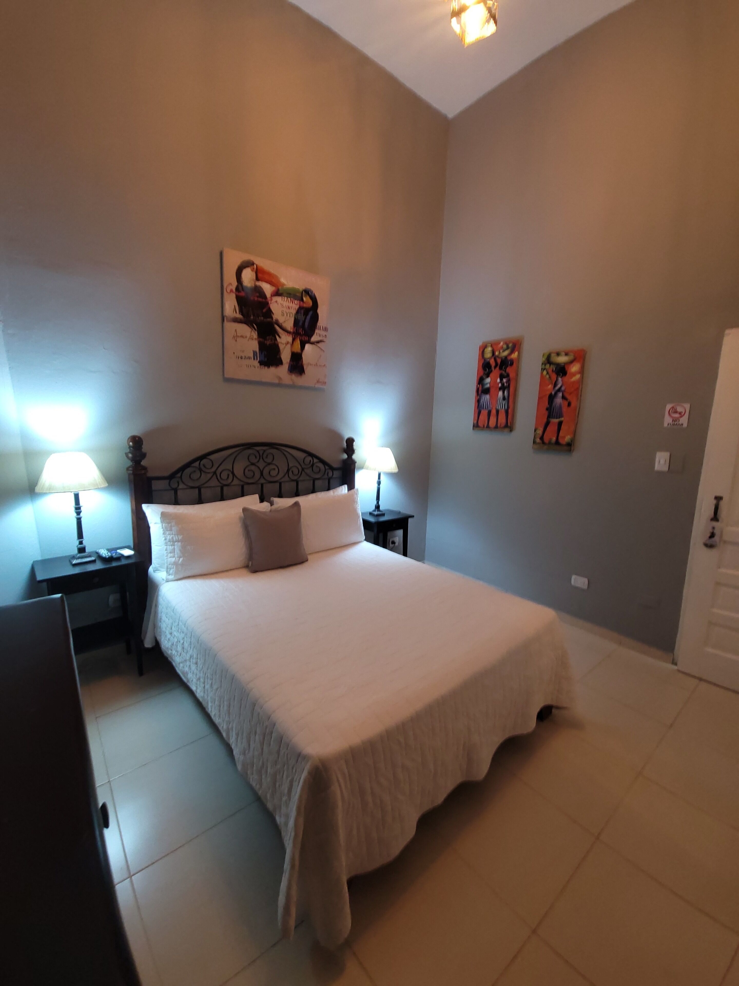 Une chambre à coucher avec un grand lit, deux tables de chevet avec des lampes, une œuvre d’art accrochée au mur et une porte.