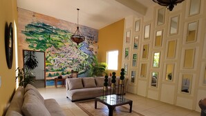 A living room with a beige sofa, a glass coffee table, and a mural on the wall. - Hotel Class Colonial (Santo Domingo)