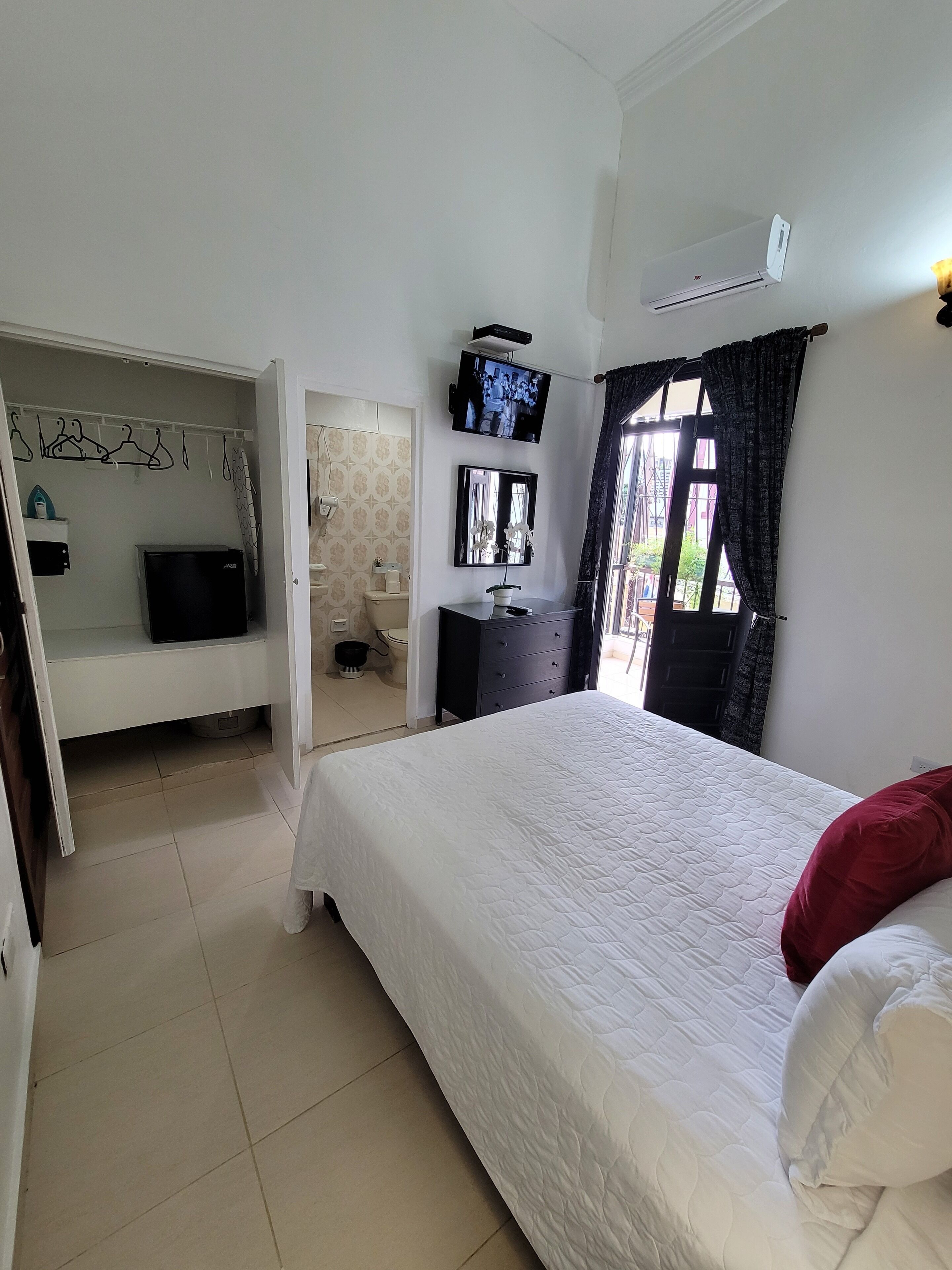 A bedroom with a bed, a TV, a wardrobe, and a bathroom visible through an open door.