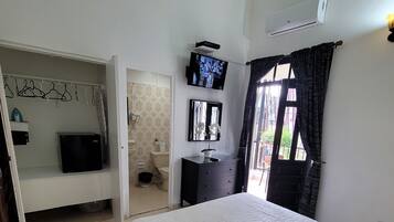 Quarto com cama, televisão, guarda-roupa e banheiro visível através de uma porta aberta.
