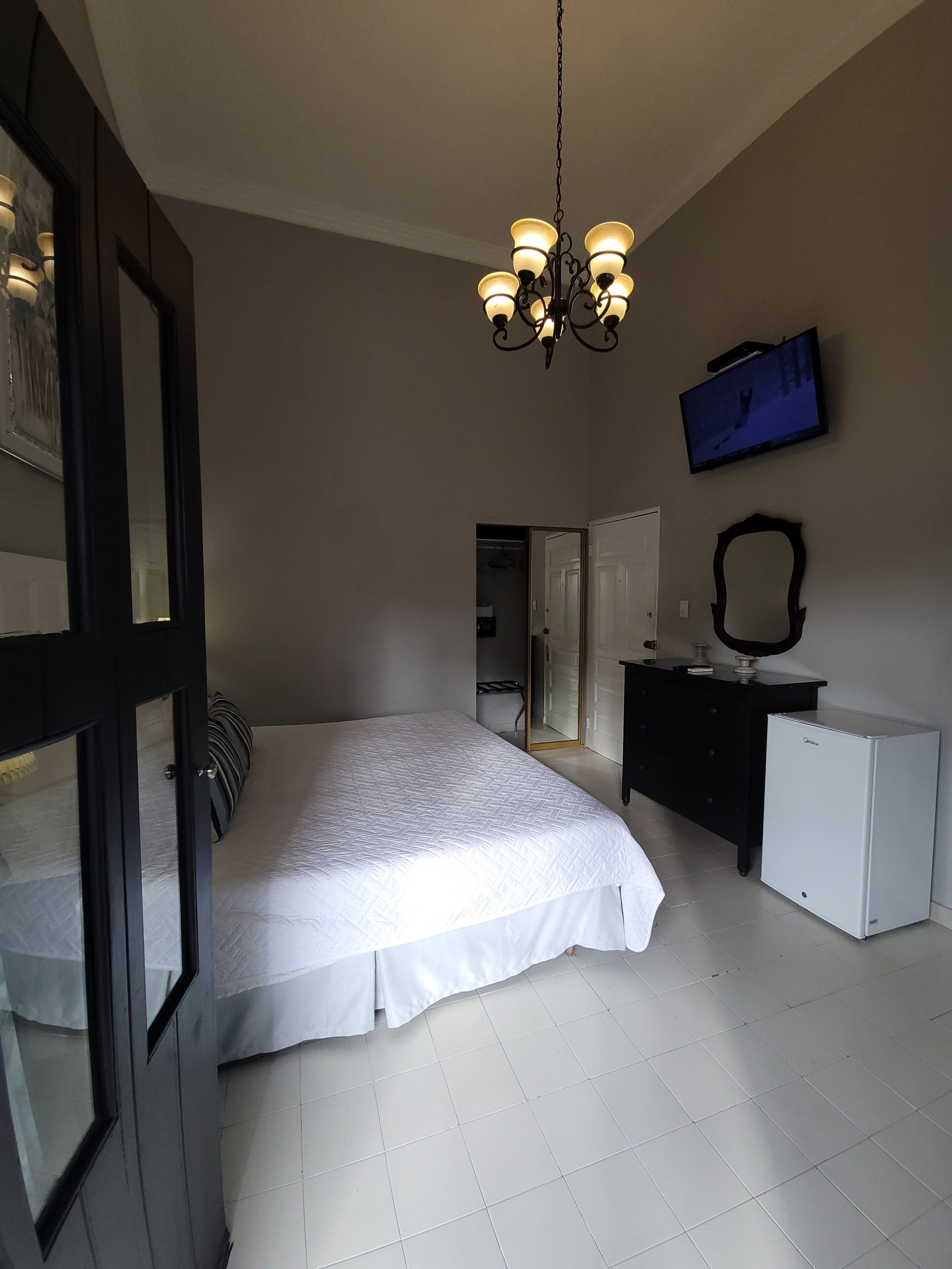 A bedroom with a bed, a dresser, a television, and a refrigerator.