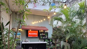 An outdoor seating area with tables and chairs, a bar with a 'Bossa Latorino' sign, and various plants. - Hotel Class Colonial (Santo Domingo)