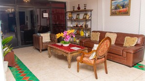 Una sala de estar con un sofá de cuero marrón, una mesa de centro de madera con mantel rojo, una estantería y un cuadro en la pared.