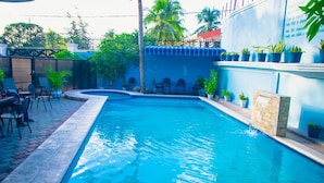 Una piscina con borde de azulejos, rodeada de sillas y plantas en macetas.