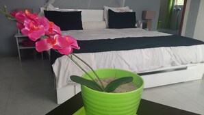 A hotel room with a bed, a green potted plant, and a nightstand. - The Sanctuary (Mahavelona)