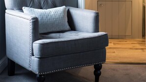 A room with a grey upholstered armchair, a wooden wall, a bathroom with a sink and mirror, and a framed deer artwork on the wall. - Kilchrenan Inn (Taynuilt)