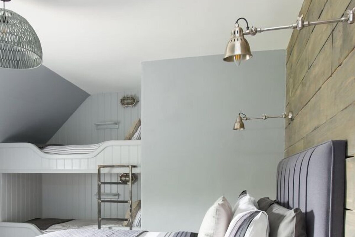 A bedroom with a bunk bed, a large bed with a headboard, and a hanging light fixture.