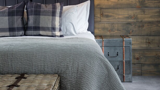 A bedroom with a wooden headboard, a bed with a checkered blanket, a bedside lamp, and a small chest of drawers. - Kilchrenan Inn (Taynuilt)