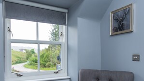 A room with a grey upholstered armchair, a window with a view of greenery, and a framed picture on the wall. - Kilchrenan Inn (Taynuilt)