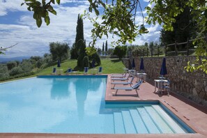 Une piscine entourée de murs de pierre et de verdure, avec des chaises longues et des parasols.
