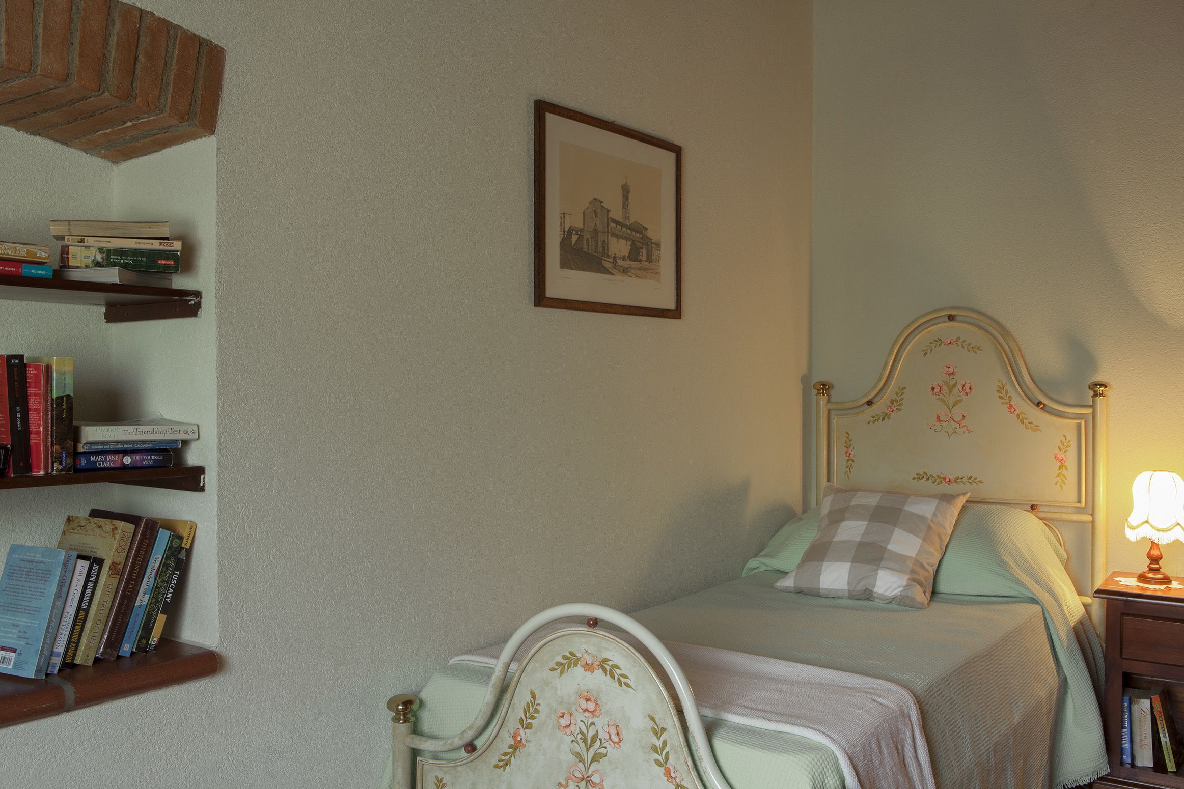 A bedroom with a bed, a nightstand, a lamp, a bookshelf, and a framed picture on the wall.
