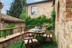 Un bâtiment en pierre avec un toit en tuiles, une table en bois dressée pour le repas et une chaise en bois.