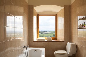 A bathroom with a bathtub, toilet, and a window with a view of a landscape. - Quercia Al Poggio (Barberino Tavarnelle)
