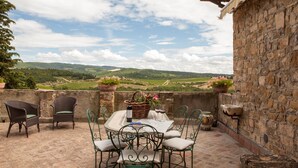 A patio with wicker chairs and a table set for two, overlooking a vineyard. - Quercia Al Poggio (Barberino Tavarnelle)