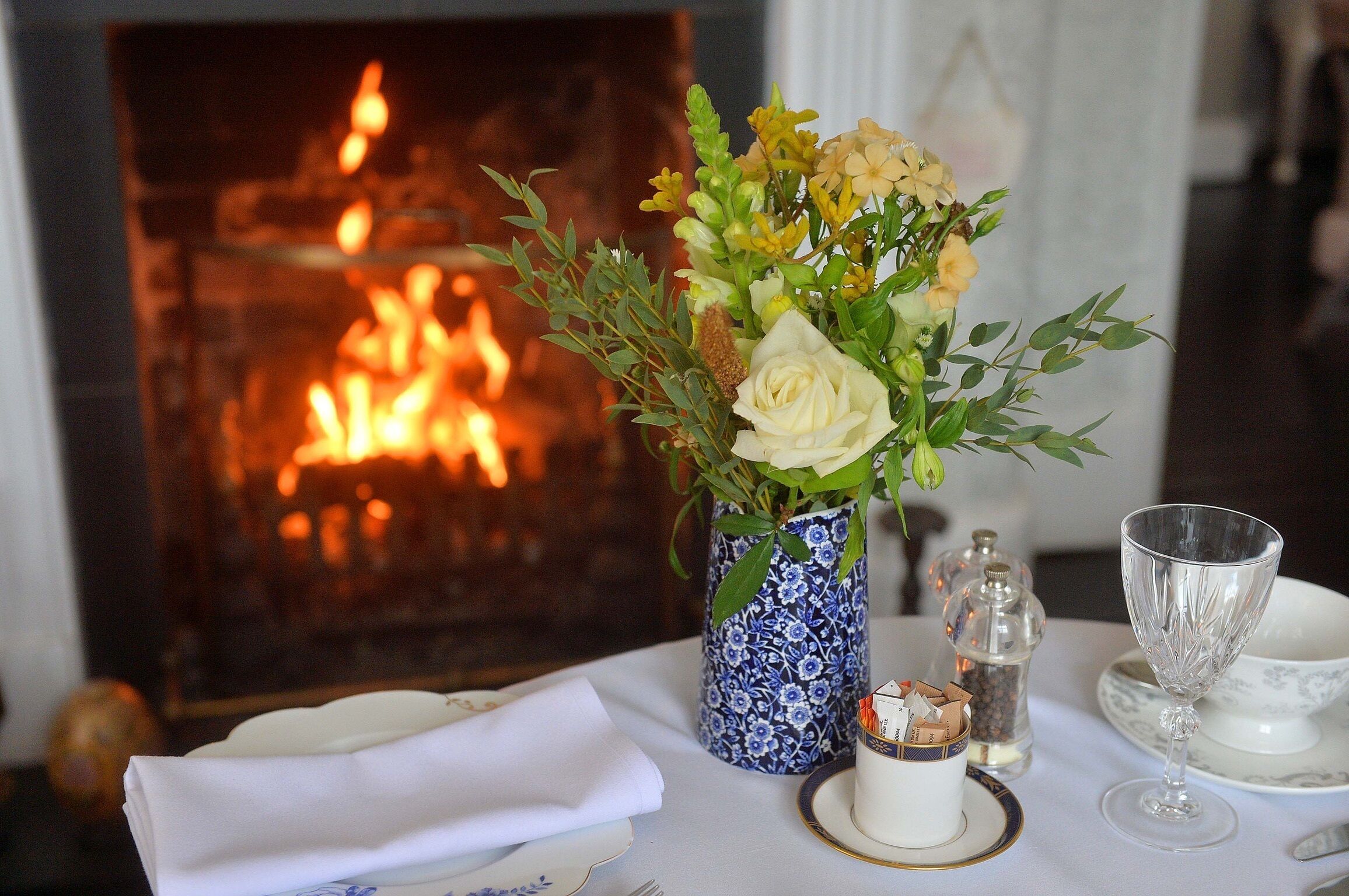 Una mesa de comedor dispuesta con un florero, un salero y pimentero, una copa y una taza de té.