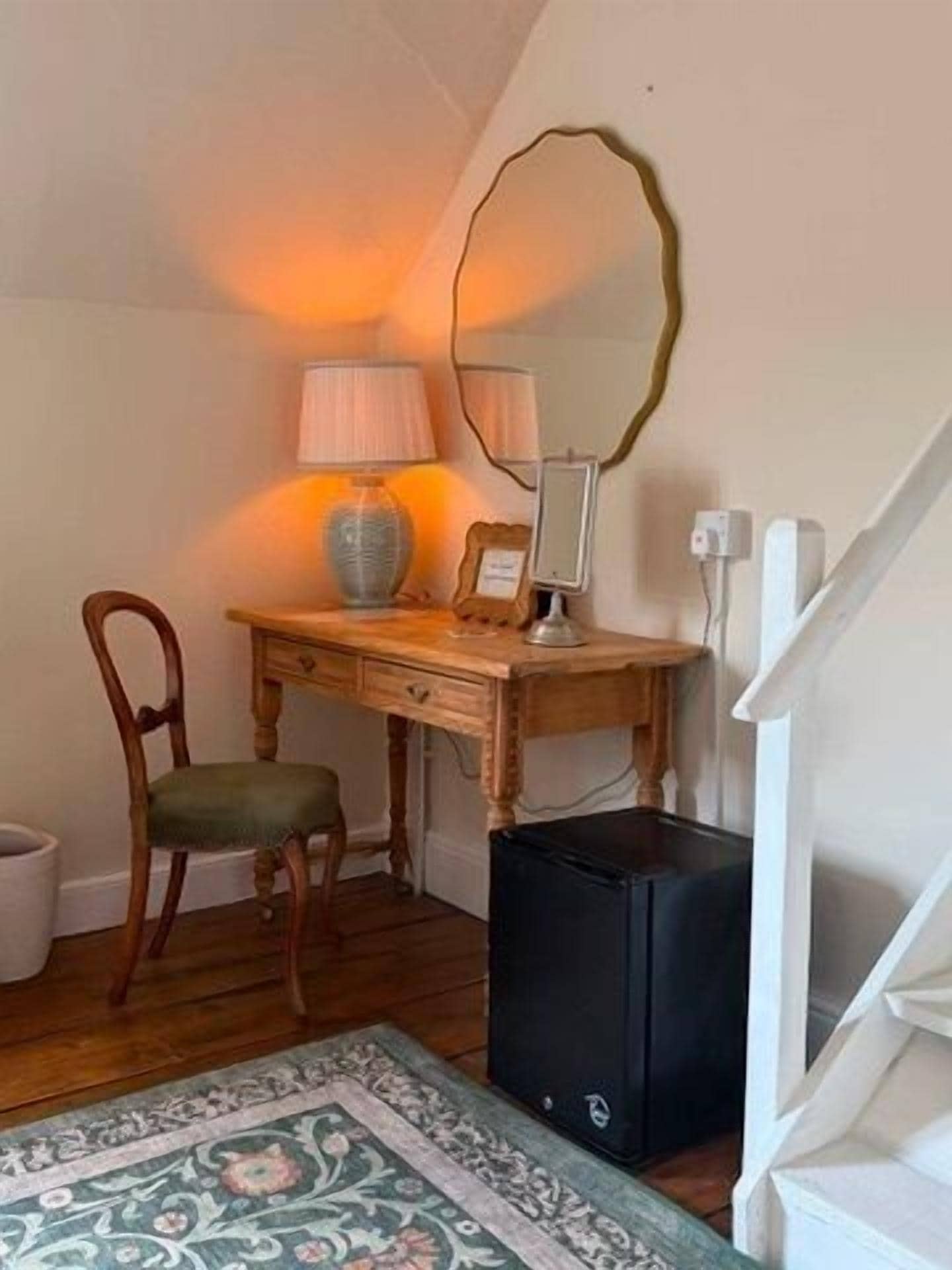 A room with a desk, chair, lamp, mirror, and a black speaker.