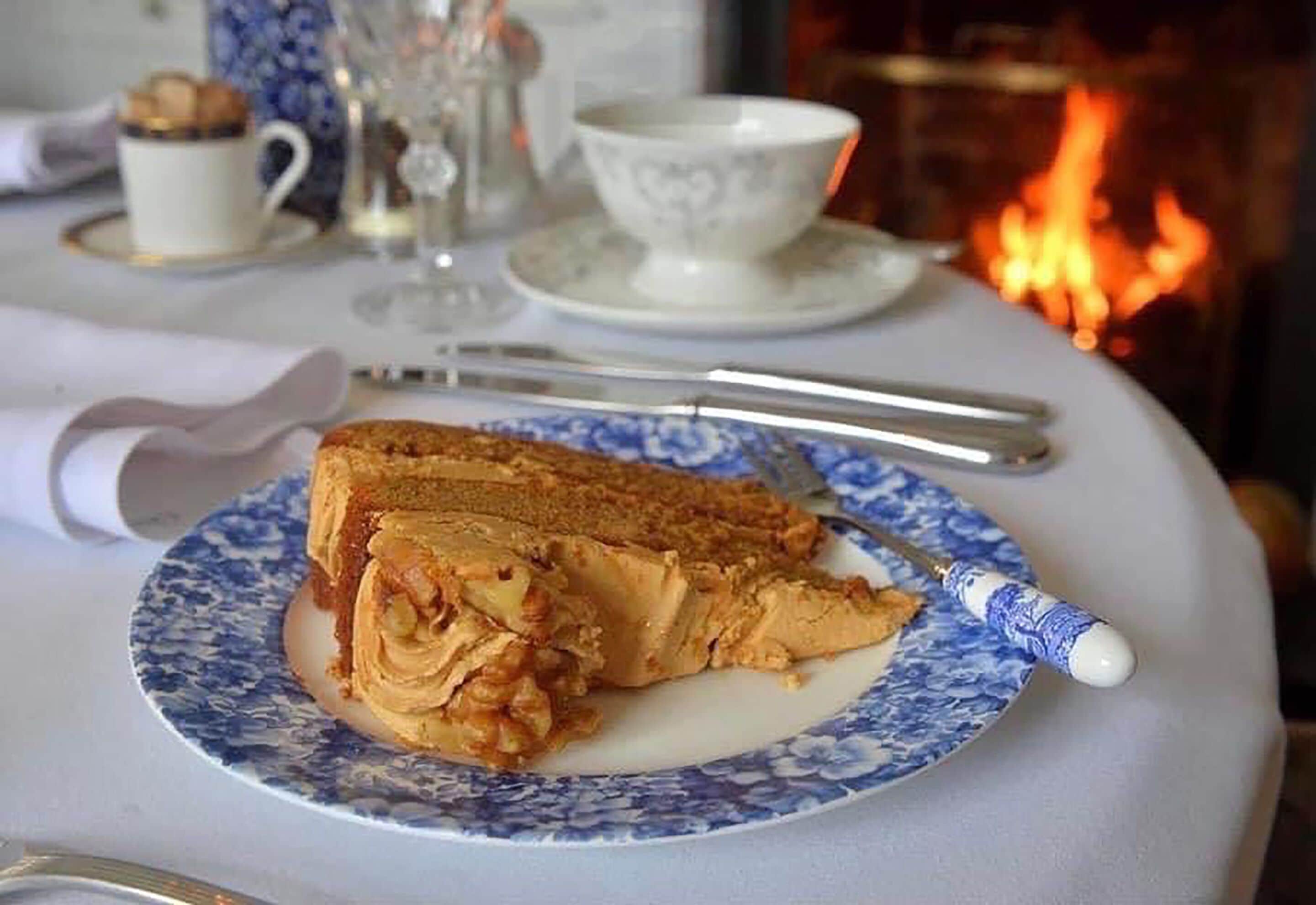 Un dessert présenté sur une assiette à motifs bleus, une tasse, une théière et une cheminée en arrière-plan.