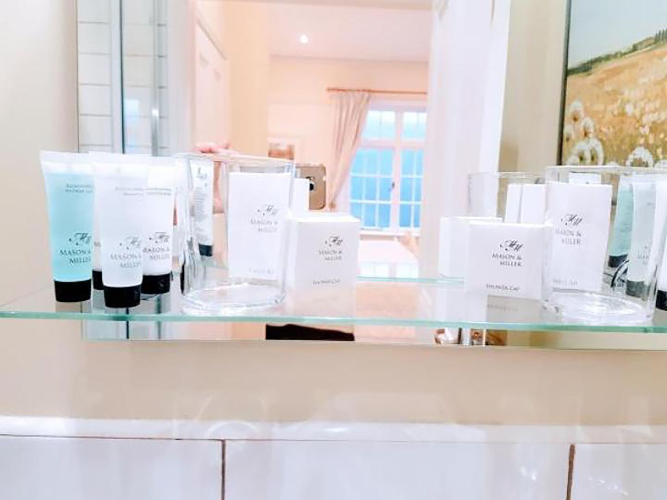 A bathroom with a glass shelf displaying various skincare products.