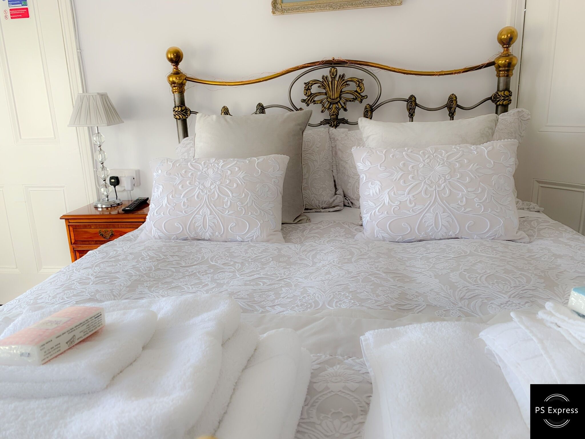A neatly made bed with a decorative headboard, a bedside table with a lamp, and a wall-mounted power outlet.