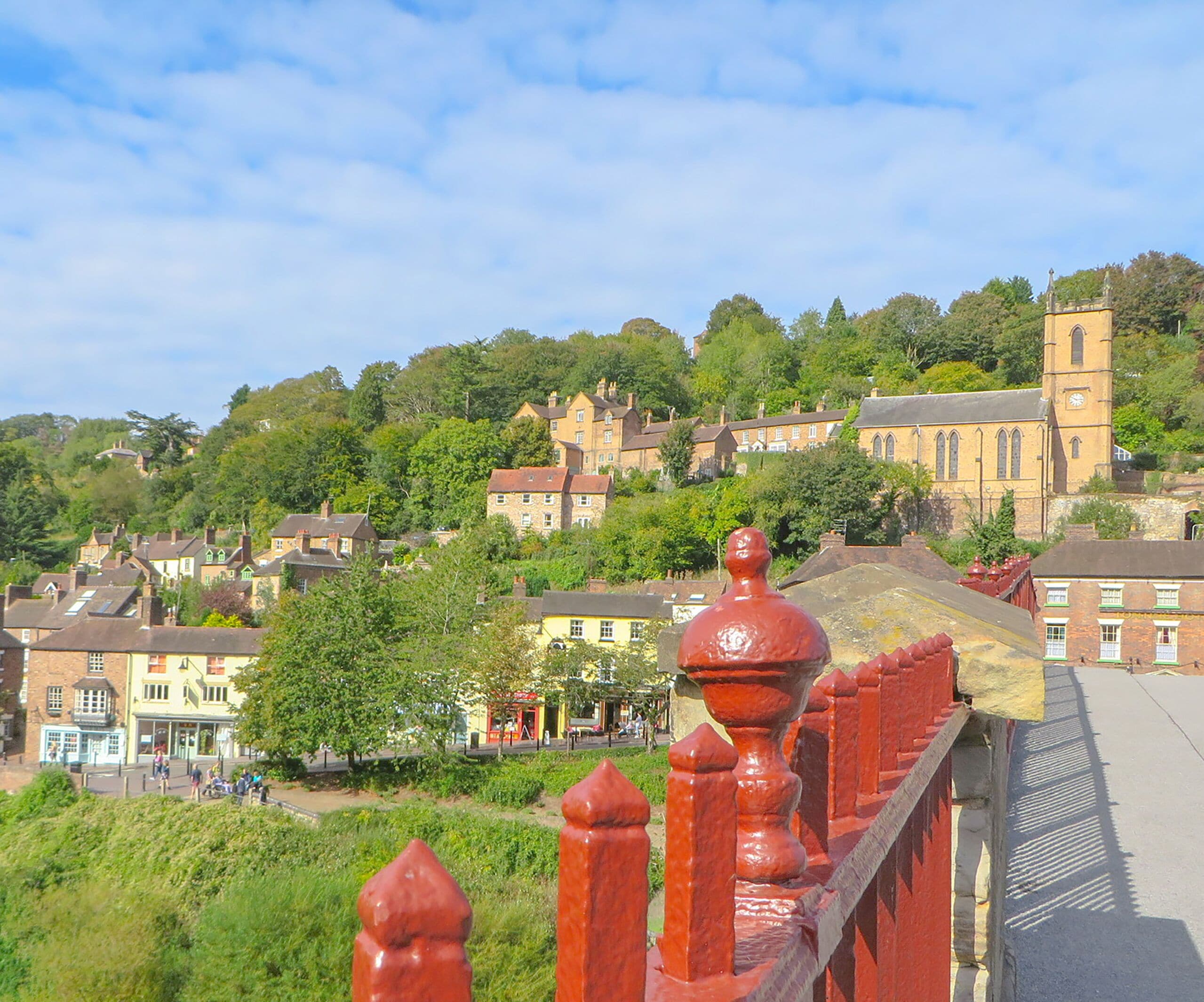 A red metal fence with a balustrade overlooking a town with historic buildings and a church on a hill.