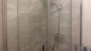 Une douche fermée par des parois en verre, dotée d’un pommeau de douche à main et d’un robinet mural.