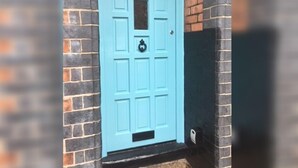 Una puerta azul claro con el número 5, ubicada en una pared de ladrillo.