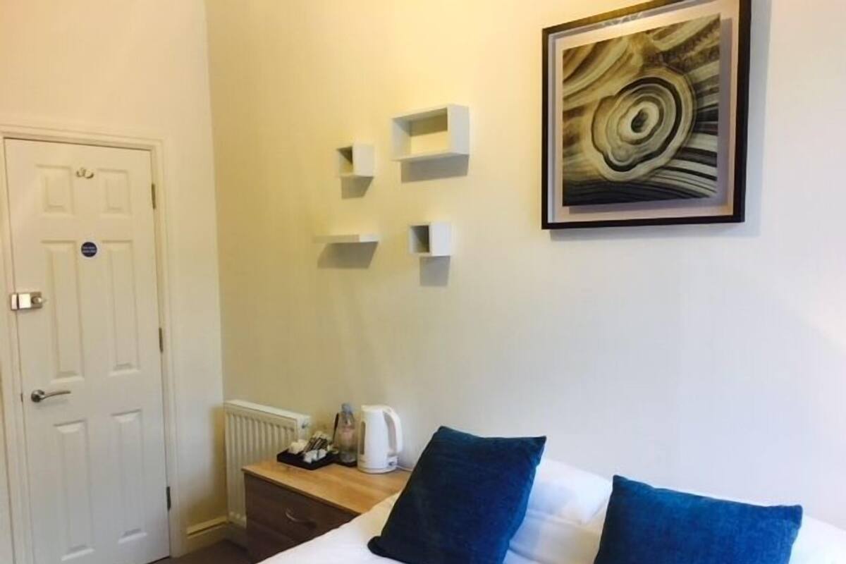 Una habitación de hotel con cama, radiador, cafetera y un cuadro en la pared.