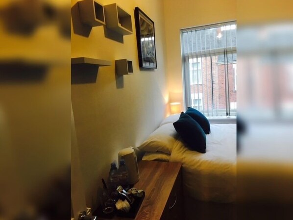 Habitación de hotel con una cama, una mesita de noche con una botella y vasos, una ventana con vistas a edificios y una pared con decoración geométrica.