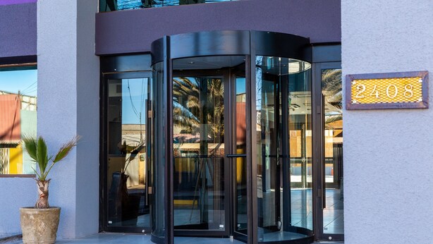 A modern building entrance with a revolving door, a potted plant, and a sign displaying the number 2408. - Hotel Modular Express Calama (Calama)