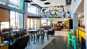 A modern dining area with tables and chairs, a mural on the wall, and large windows. - Hotel Modular Express Calama (Calama)
