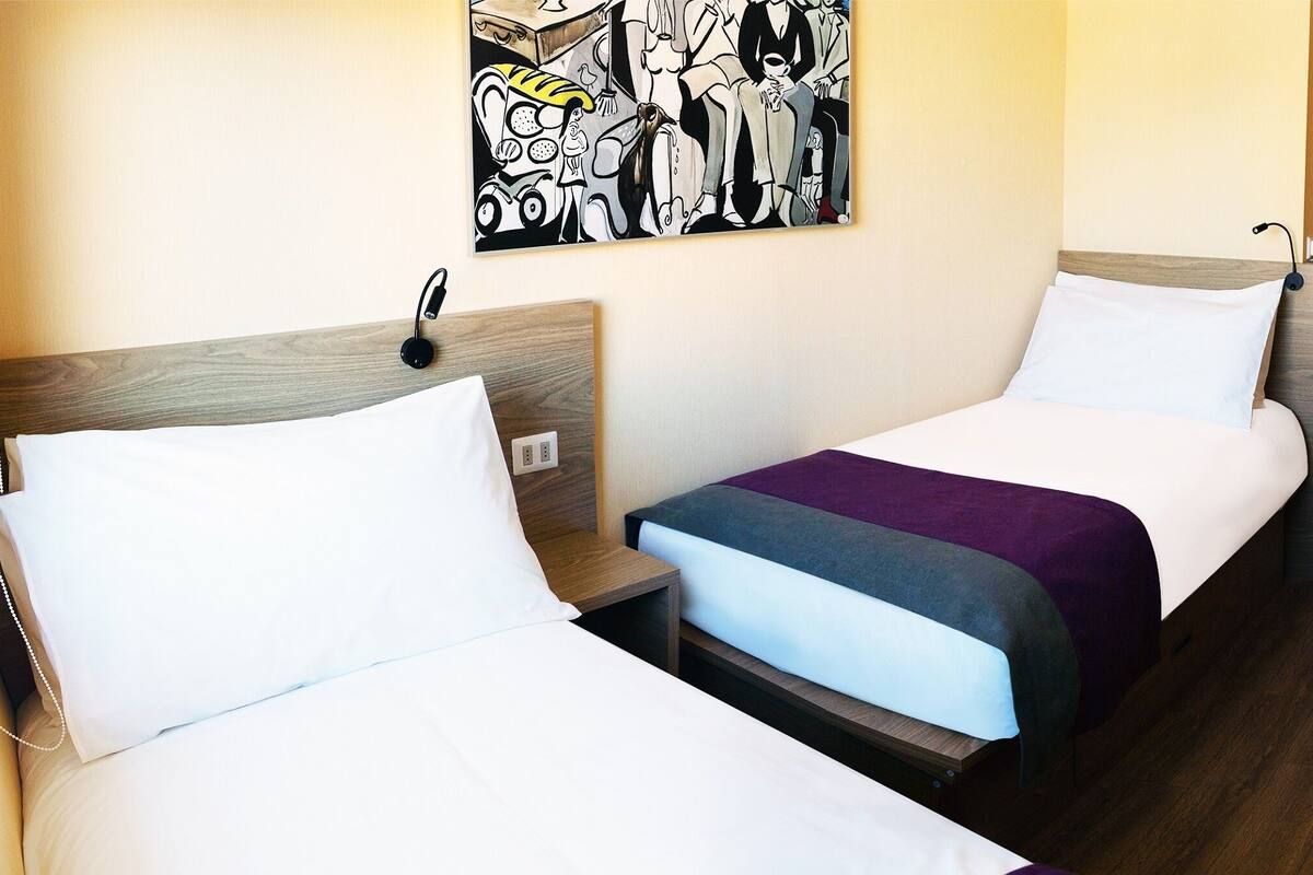 Habitación de hotel con dos camas, un escritorio con una computadora portátil y un cuadro en la pared.