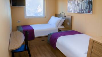 A compact hotel room with two single beds, a small desk, and a chair.