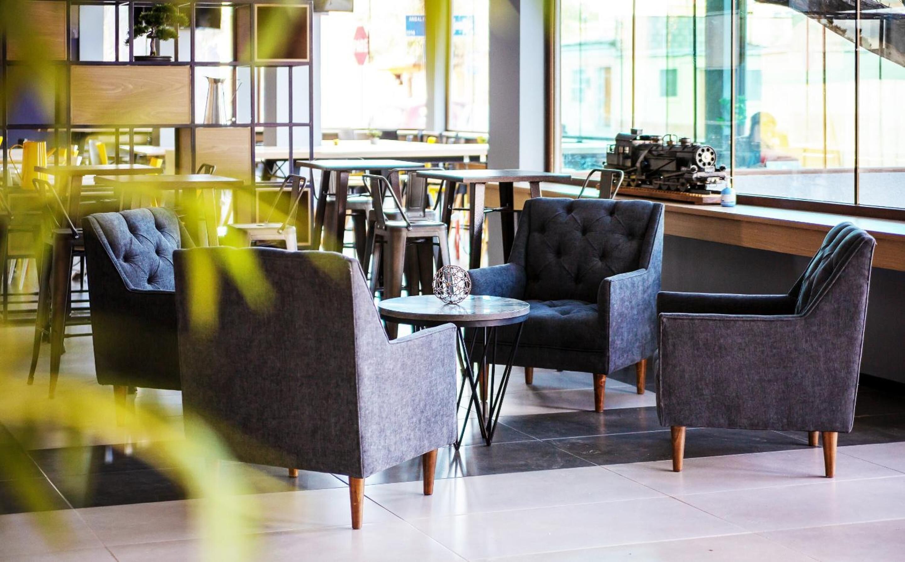 A modern cafe with dark upholstered chairs, a round table, and a large window providing a view of the street.