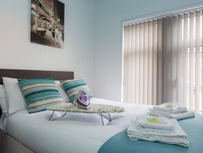 Una cama bien hecha con almohadillas a rayas, una plancha pequeña y toallas ordenadamente dobladas.