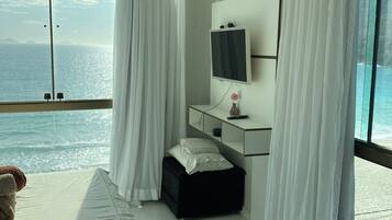 Quarto de hotel com uma cama, mesa de cabeceira, televisão e vista para o mar.